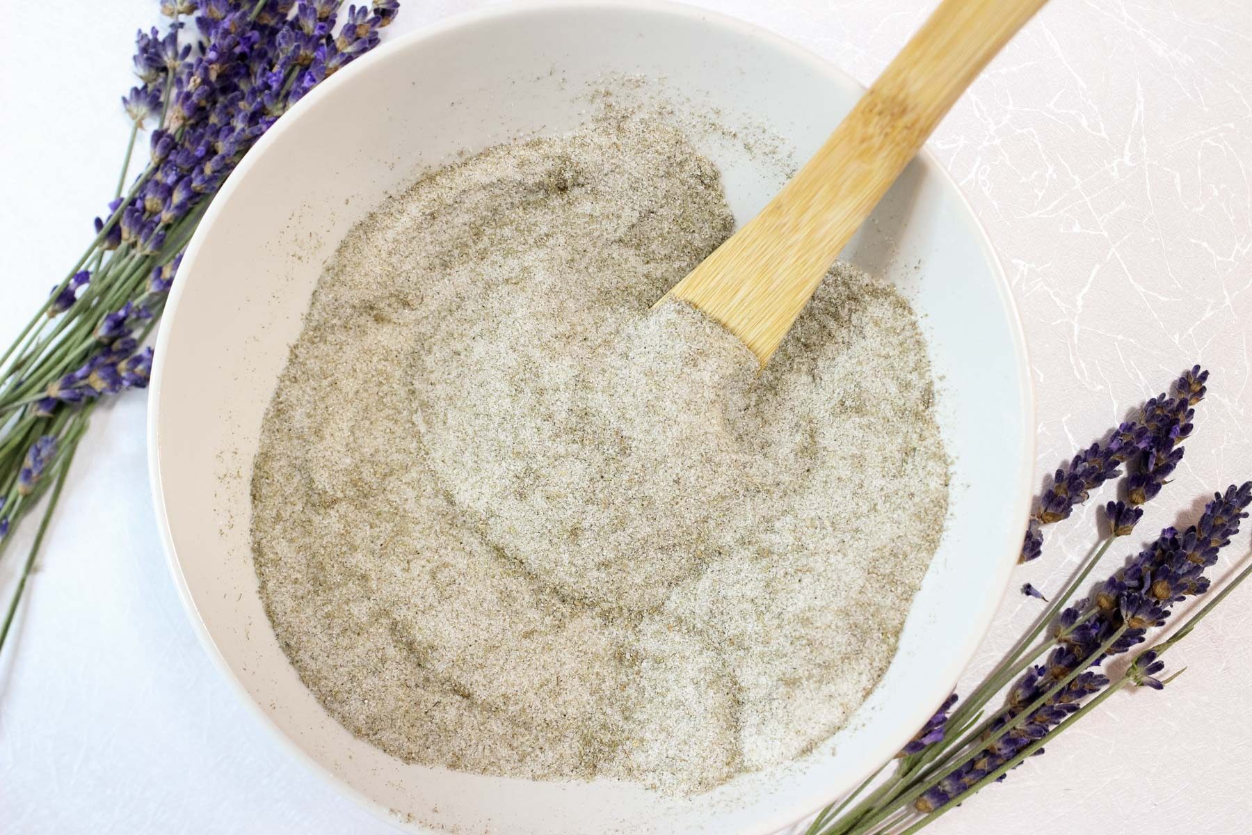 Lavender sugar in a bowl with a wood spoon.