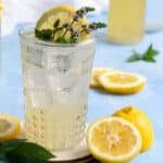 A glass with ice and homemade lemon soda with slices of lemon and fresh mint leaves.