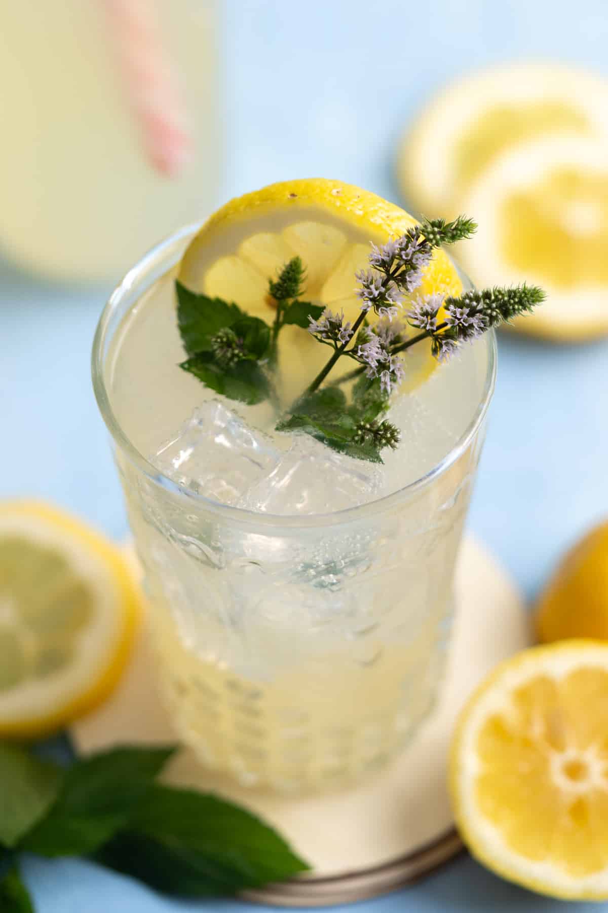 A glass with ice and homemade lemon soda with slices of lemon and fresh mint leaves.