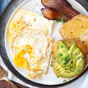 Over medium eggs on a plate with bacon and avocado toast.