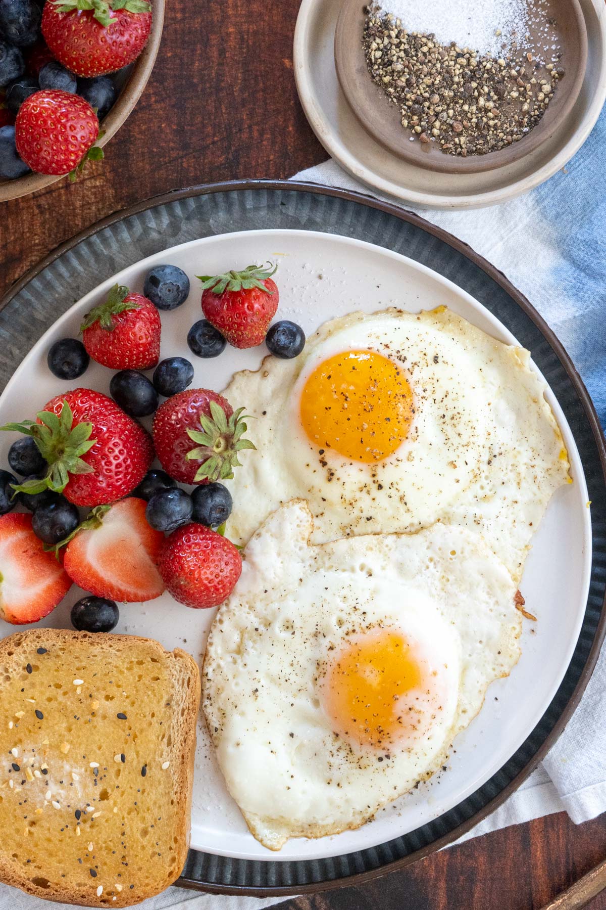 Sunny side up eggs on a plate with toast and fruit.
