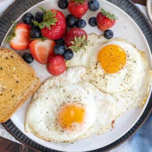 Two sunny side up eggs on a plate with toast and fruit.