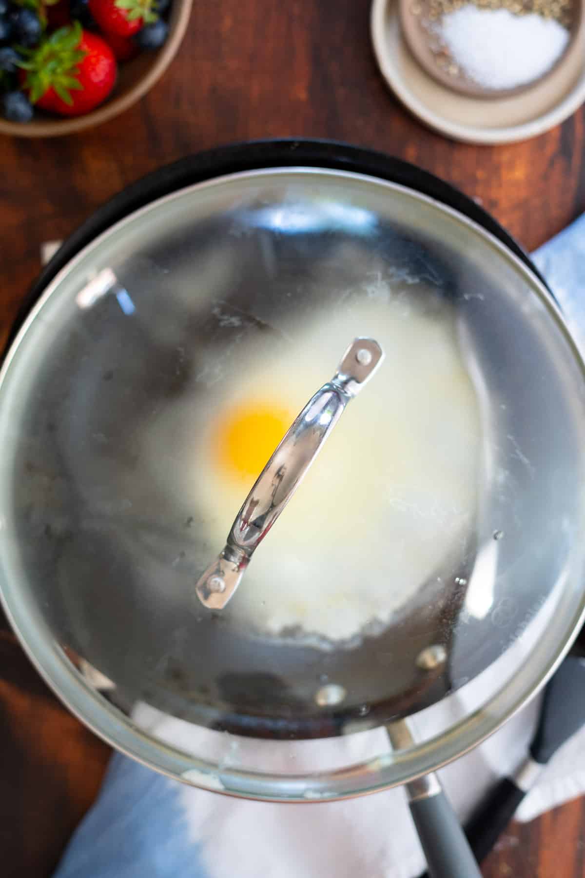 Cooking a sunny side up egg with a lid on the skillet.