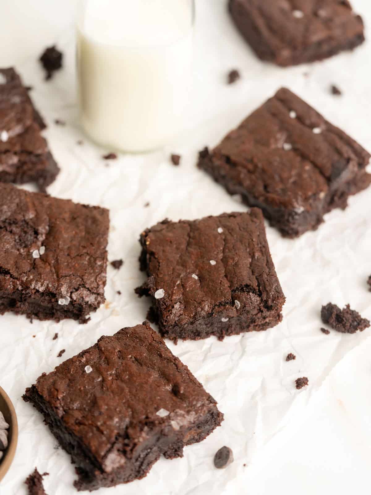 Brownies on parchment paper with a glass of milk.