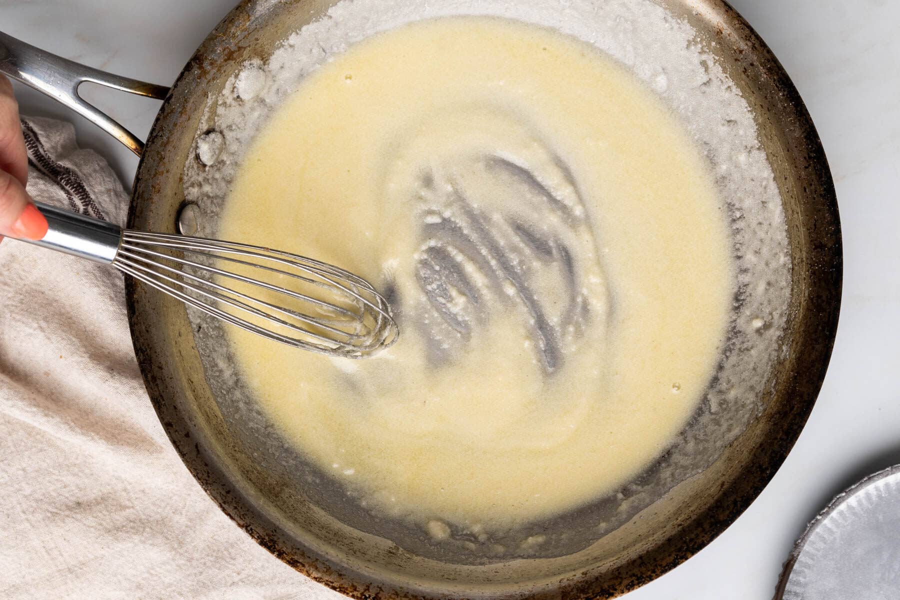 whisking a creamy gluten-free roux in a skillet on the stove, with a towel nearby for quick clean-up.