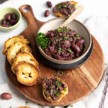 Kalamata olive tapenade in a bowl with a side of bread slices.