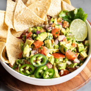 Avocado pico de gallo with chips and slice of lime.