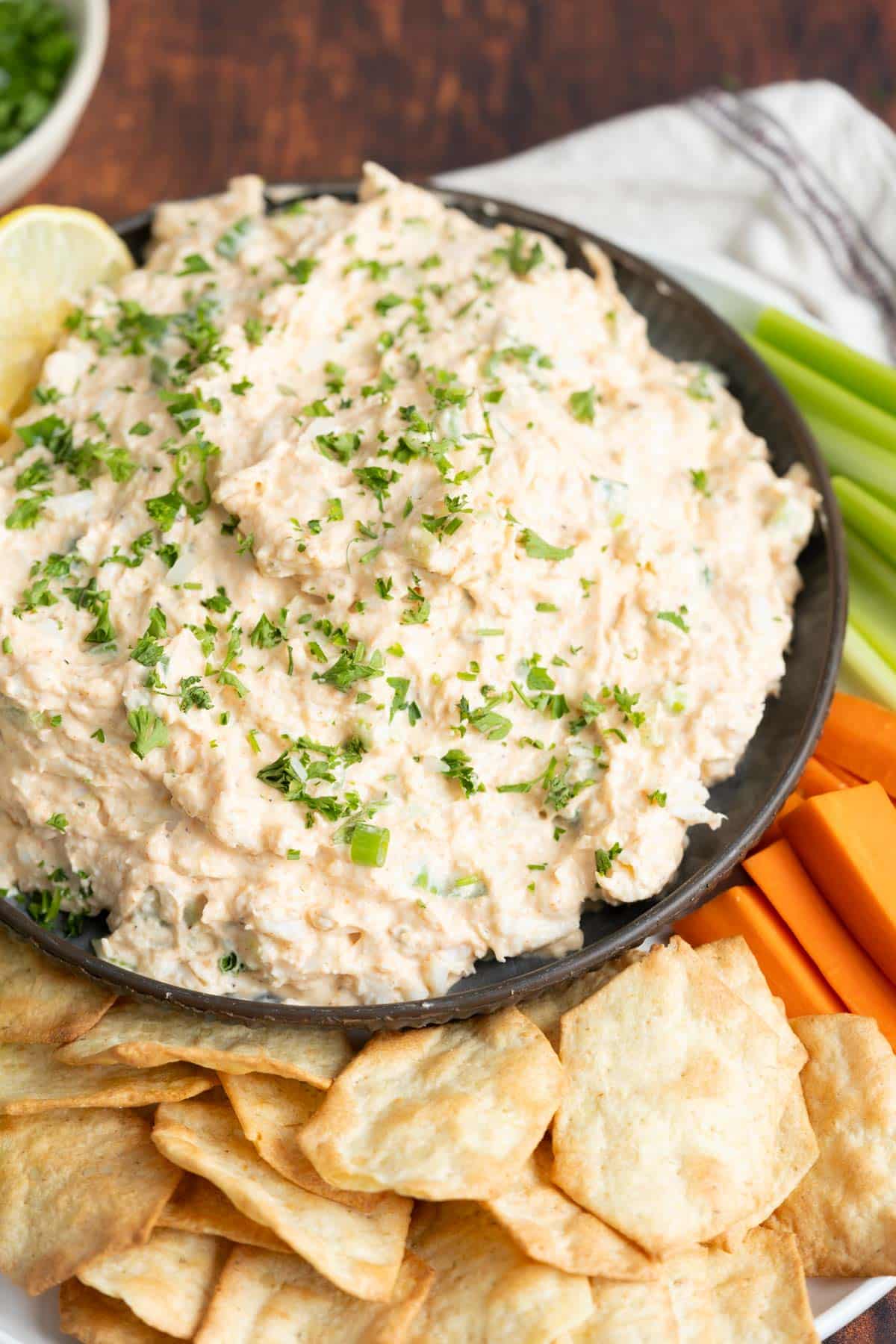 Spicy Cajun crab dip in a bowl with sides of vegetables and crackers.