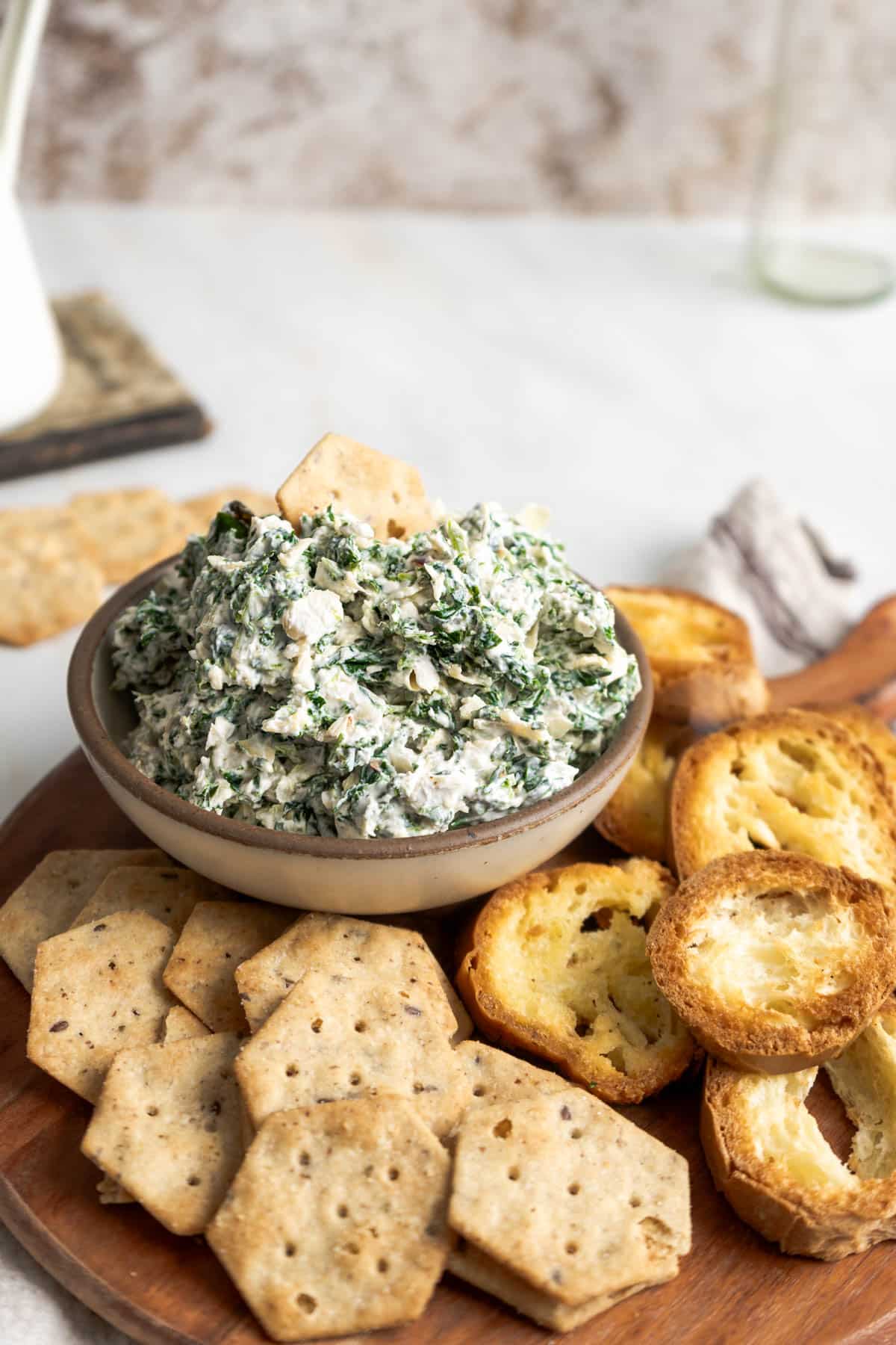 Spinach artichoke dip in a bowl with sides of bread and crackers.