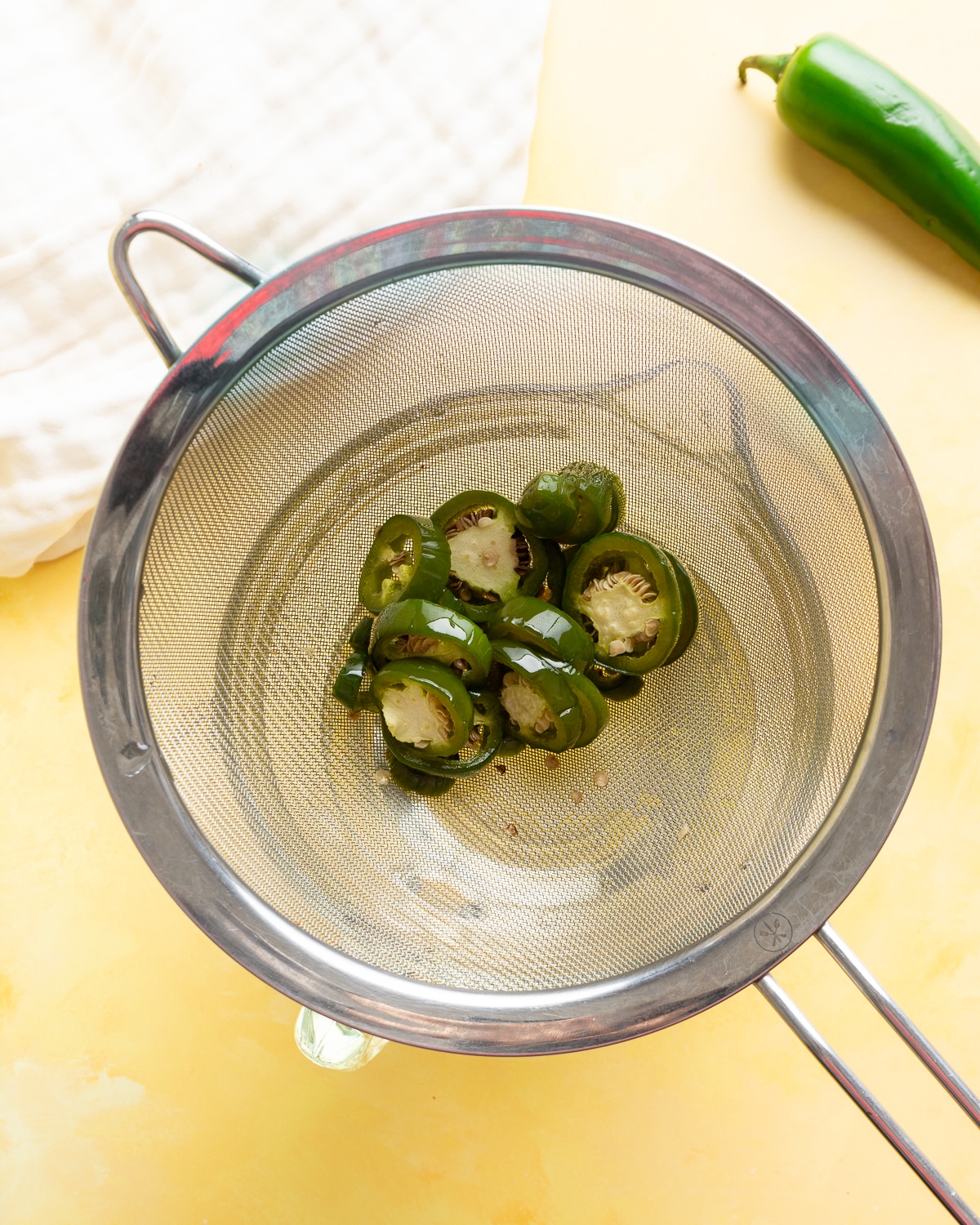 Jalapeno slices in a mesh strainer.