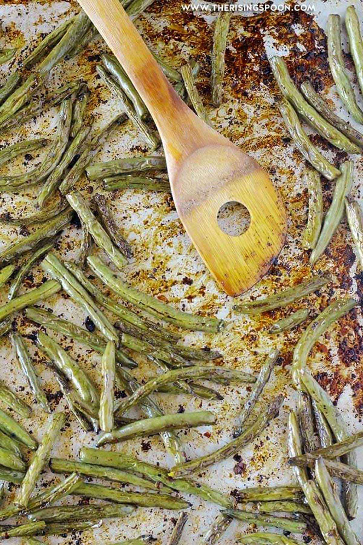 stirring green benas on sheet pan with wooden spoon