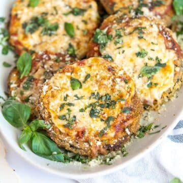 Eggplant parm topped with cheese and fresh basil on a plate.