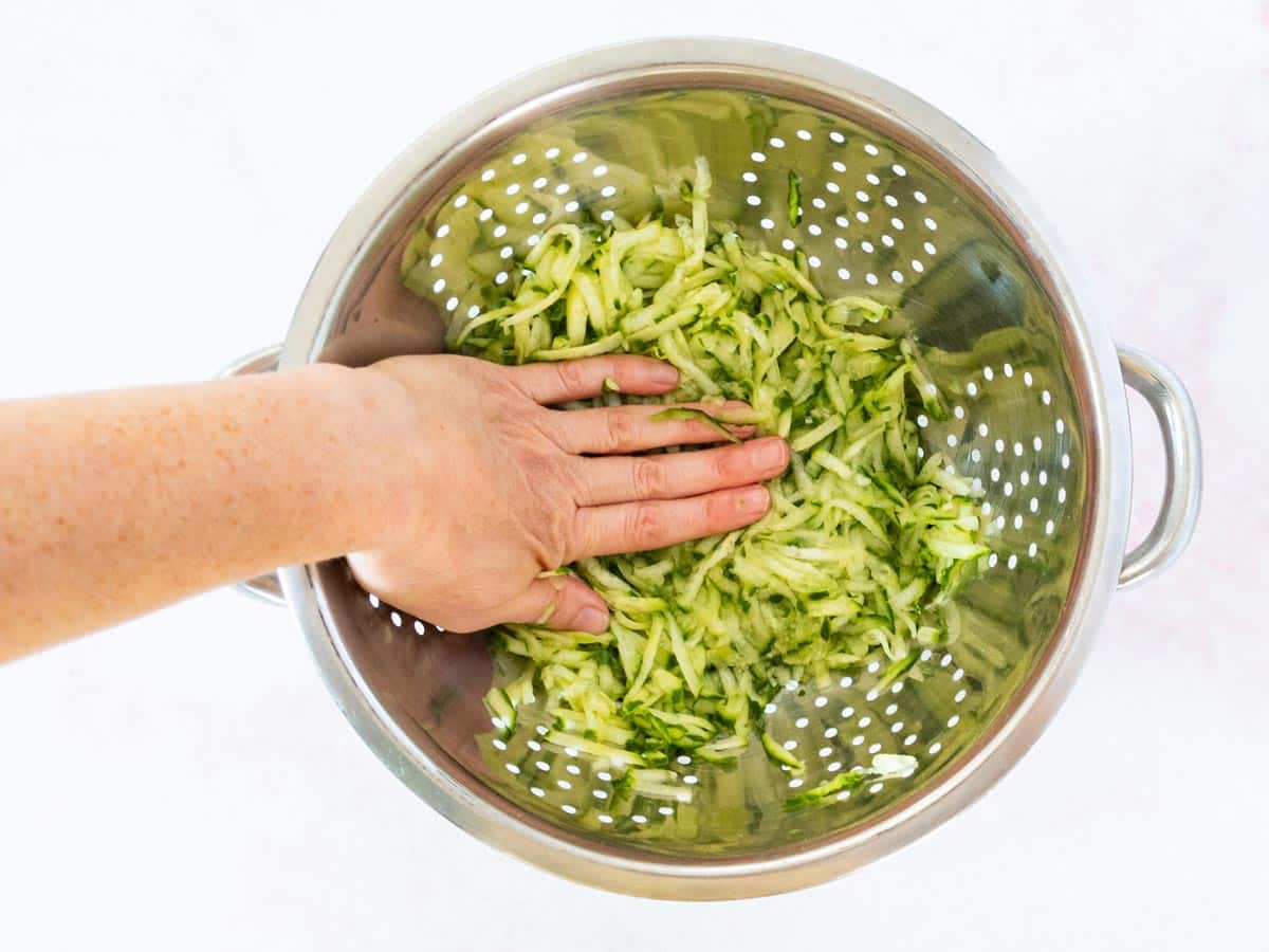 A hand pressing the cucumber down in a colander.