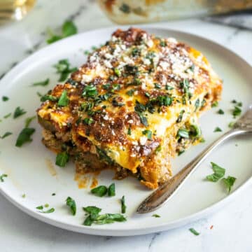 Piece of eggplant lasagna on a dinner plate with fresh basil.