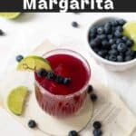 A glass of blueberry margarita garnished with a lime slice and blueberries on a fruit pick.