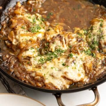 Baked chicken in a skillet topped with caramelized onions and cheese.