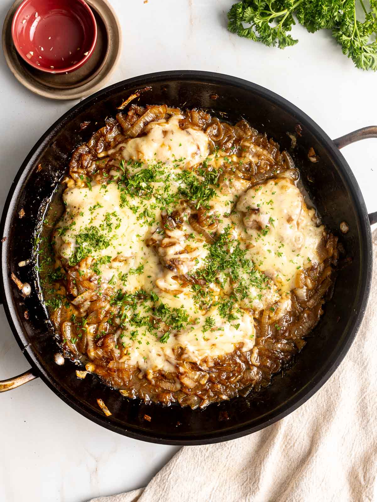 French onion chicken breast in a pan garnished with parsley.