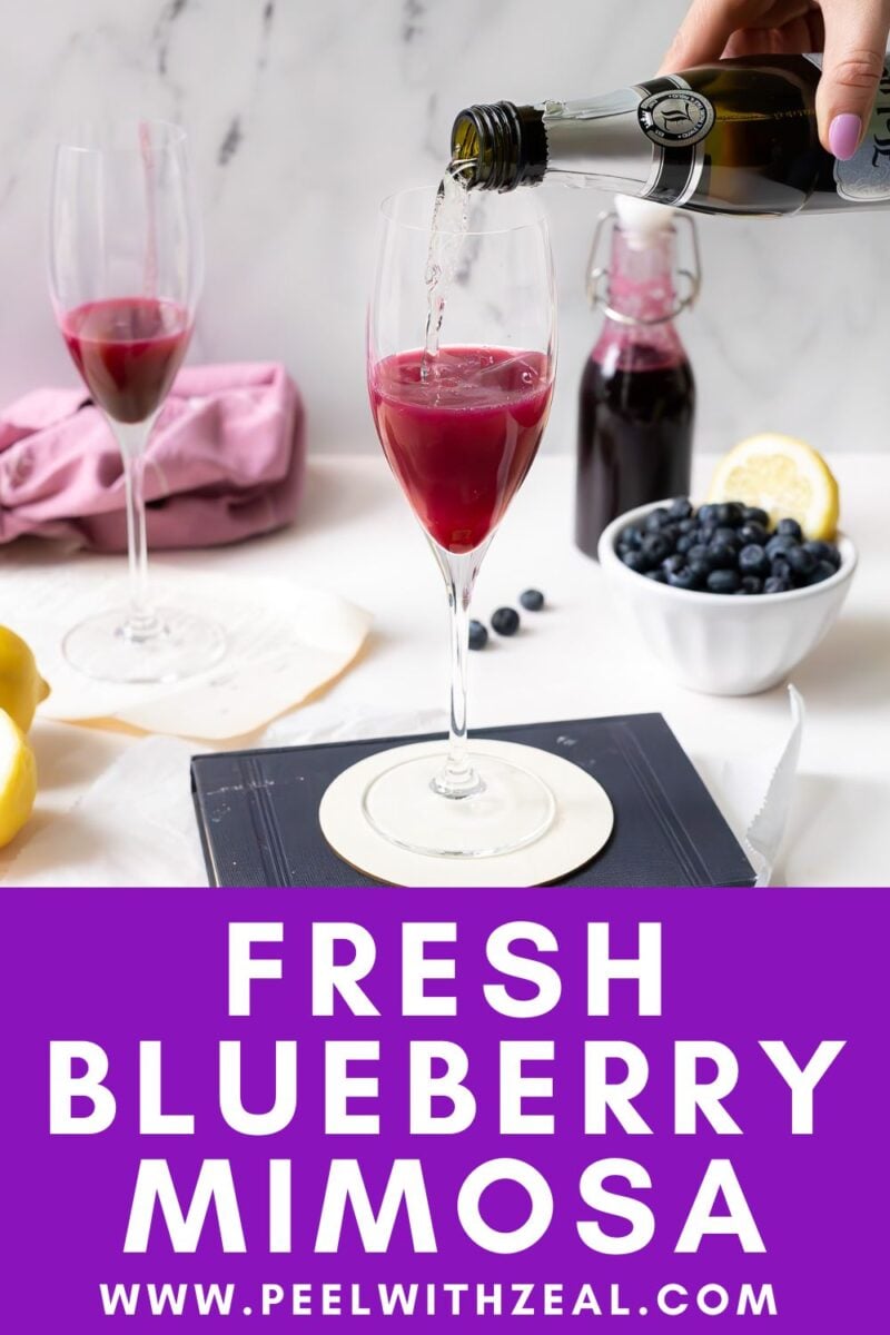Blueberry syrup in a champagne glass with prosecco being poured on top.