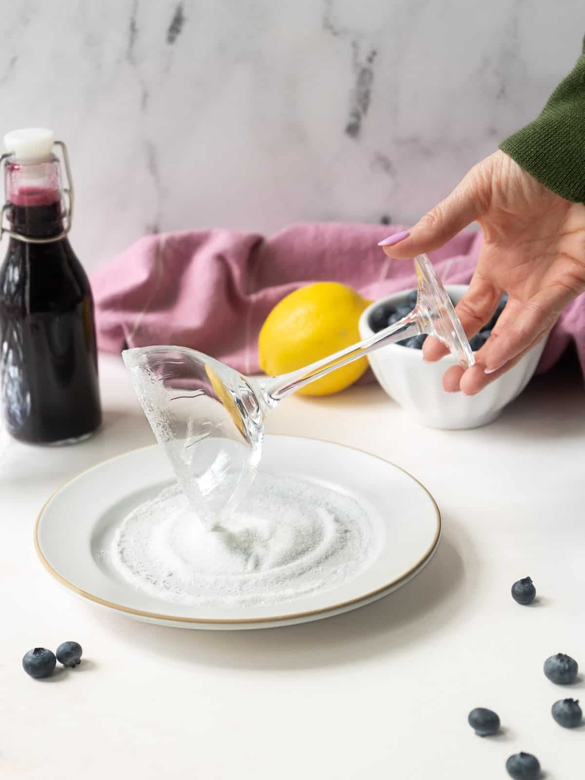 A martini glass being rimmed with salt, with a bottle of blueberry syrup in the background.⁣