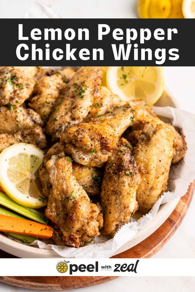 Lemon pepper chicken wings, adorned with minced parsley, lemon slices, carrot batons, and fresh parsley sprigs, on a rustic wooden platter.⁣