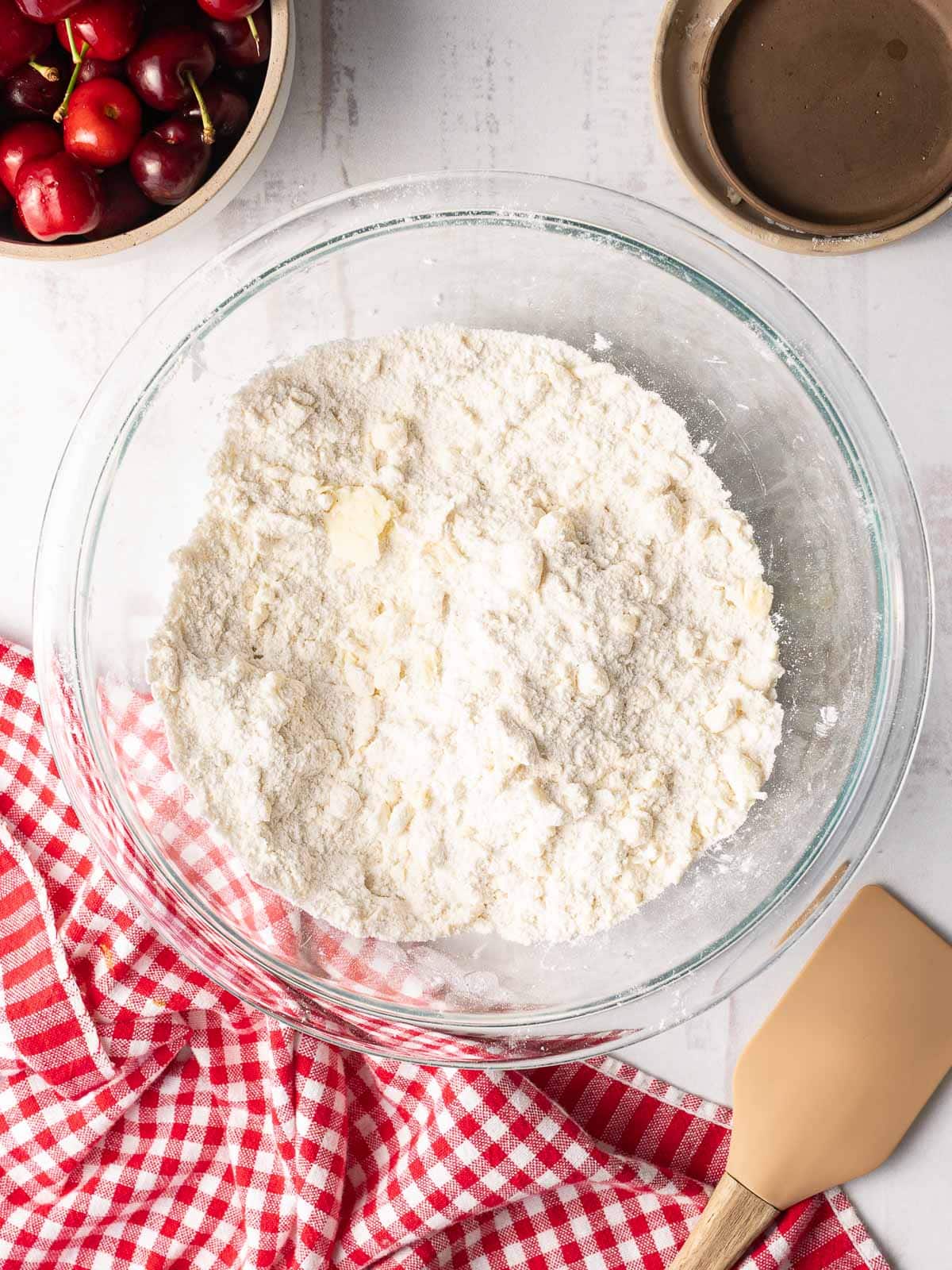 A mixing bowl containing the dry ingredients for cherry cobbler is placed on top of the table.