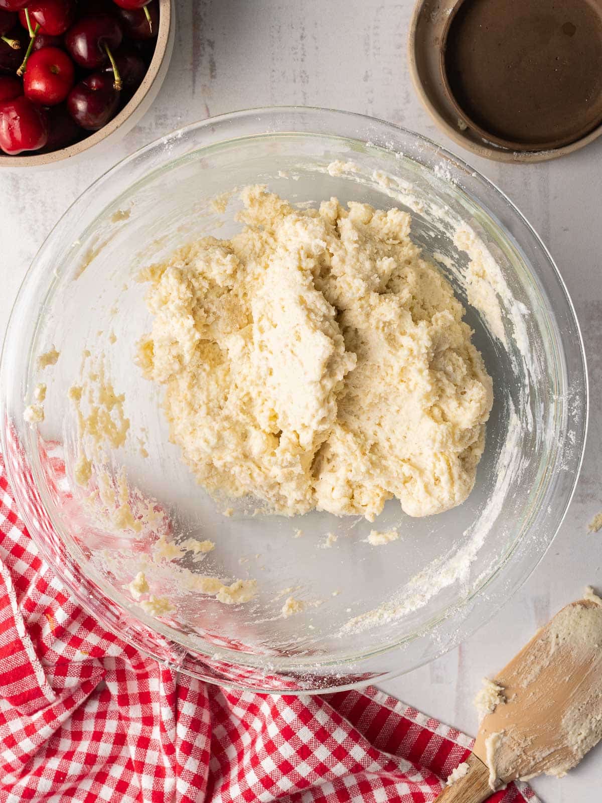 A mixing bowl containing wet and dry ingredients mixed together to form cherry cobbler batter, ready to fill the cherries, placed on top of the table.