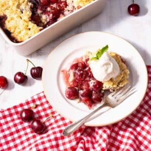A serving of gluten-free cherry cobbler topped with vanilla ice cream on a plate.⁣