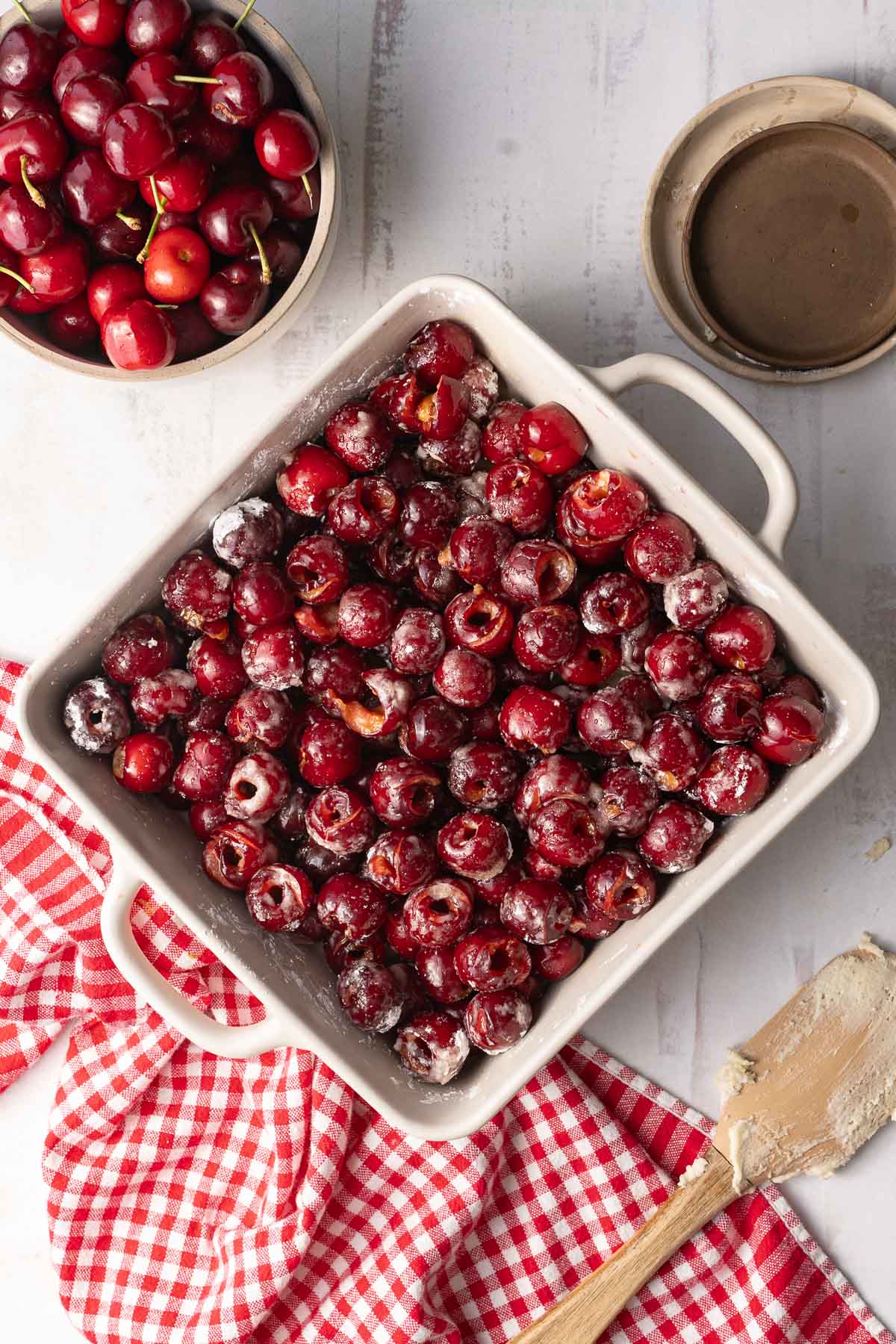 A bowl of fresh cherries and a baking dish filled with cherries, ready for cherry cobbler batter, were placed on top of the table.