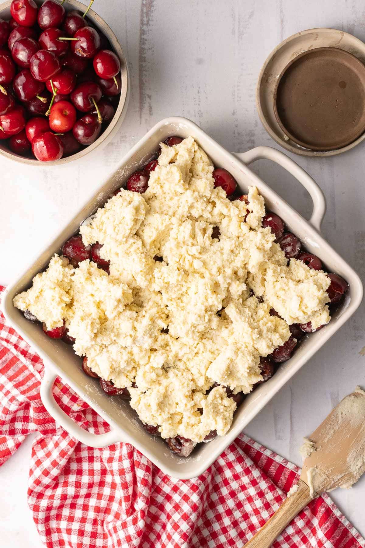 A gluten-free cherry cobbler in a baking dish, ready to bake, placed on top of the table.