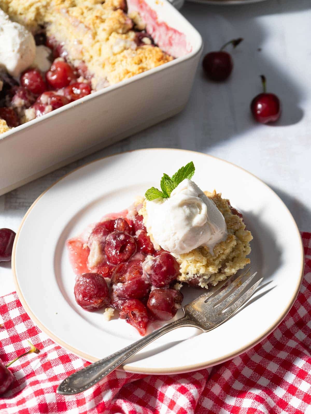 A serving of gluten-free cherry cobbler topped with vanilla ice cream on a plate.⁣