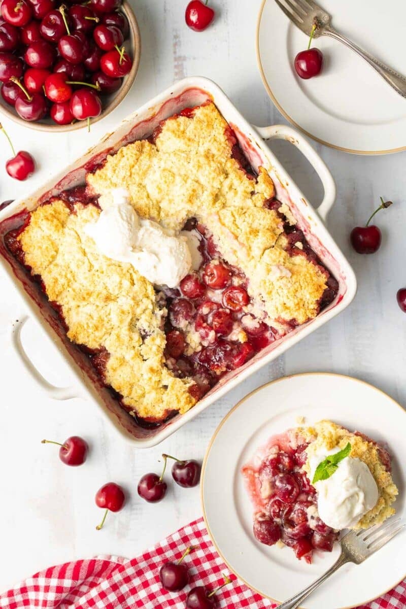 Gluten-Free Cherry Cobbler in a baking dish topped with vanilla ice cream on a table.
