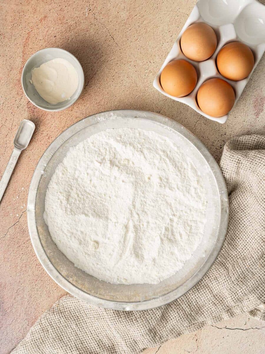 Gluten-free flour on the mixing bowl and eggs on the side sits on the tables.