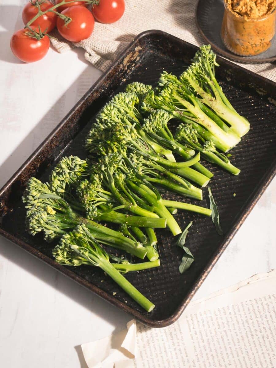 An array of fresh broccolini place on the baking sheet pan resting on the table.