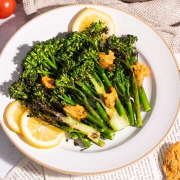 Freshly grilled broccolini serve a portion in a white dinner plate resting on the table.