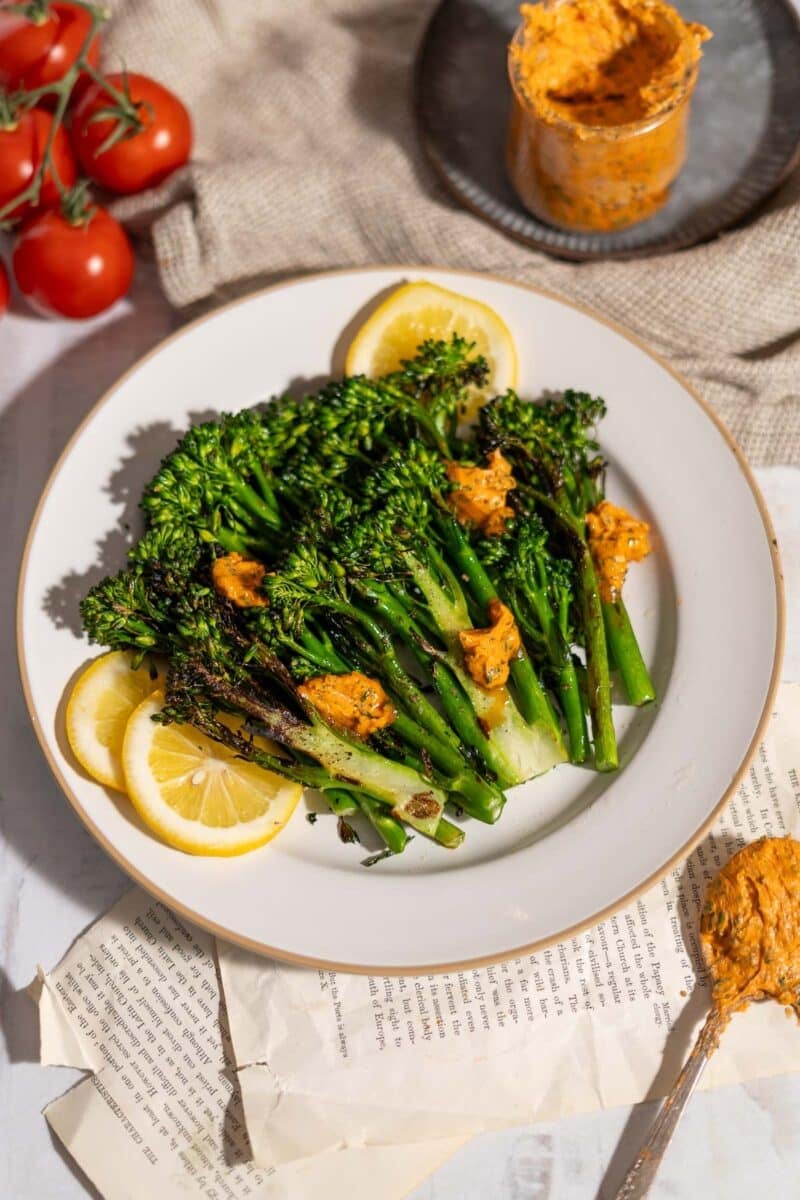 Freshly grilled broccolini plated and drizzled with tomato garlic butter garnish with lemon slices and served on the table.