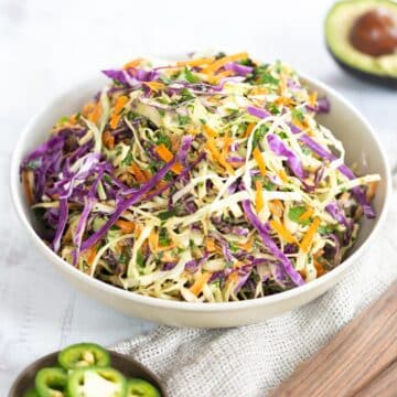 Mix of shredded carrots, green headed cabbage and purple cabbage in a salad bowl.