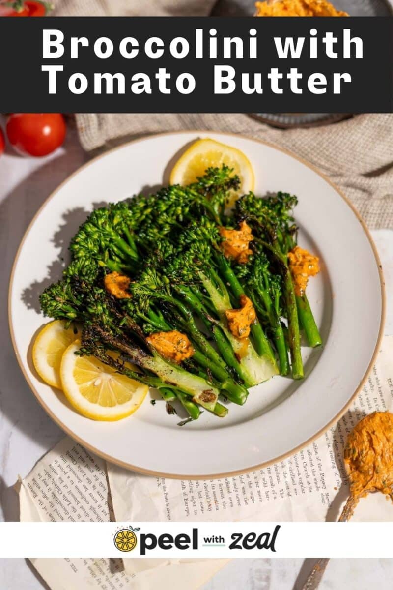 Freshly grilled broccolini plated and drizzled with tomato garlic butter garnish with lemon slices and served on the table.
