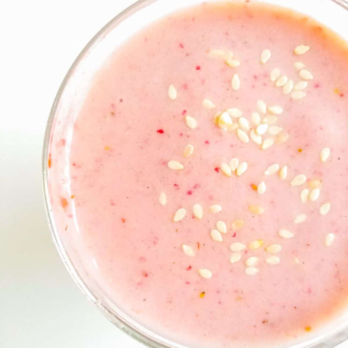 Strawberry smoothie in a glass with sesame seeds sprinkled on top. 