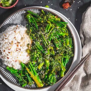 Stir fried broccolini with rice garnish with sesame seeds and some chili flakes served on a table.