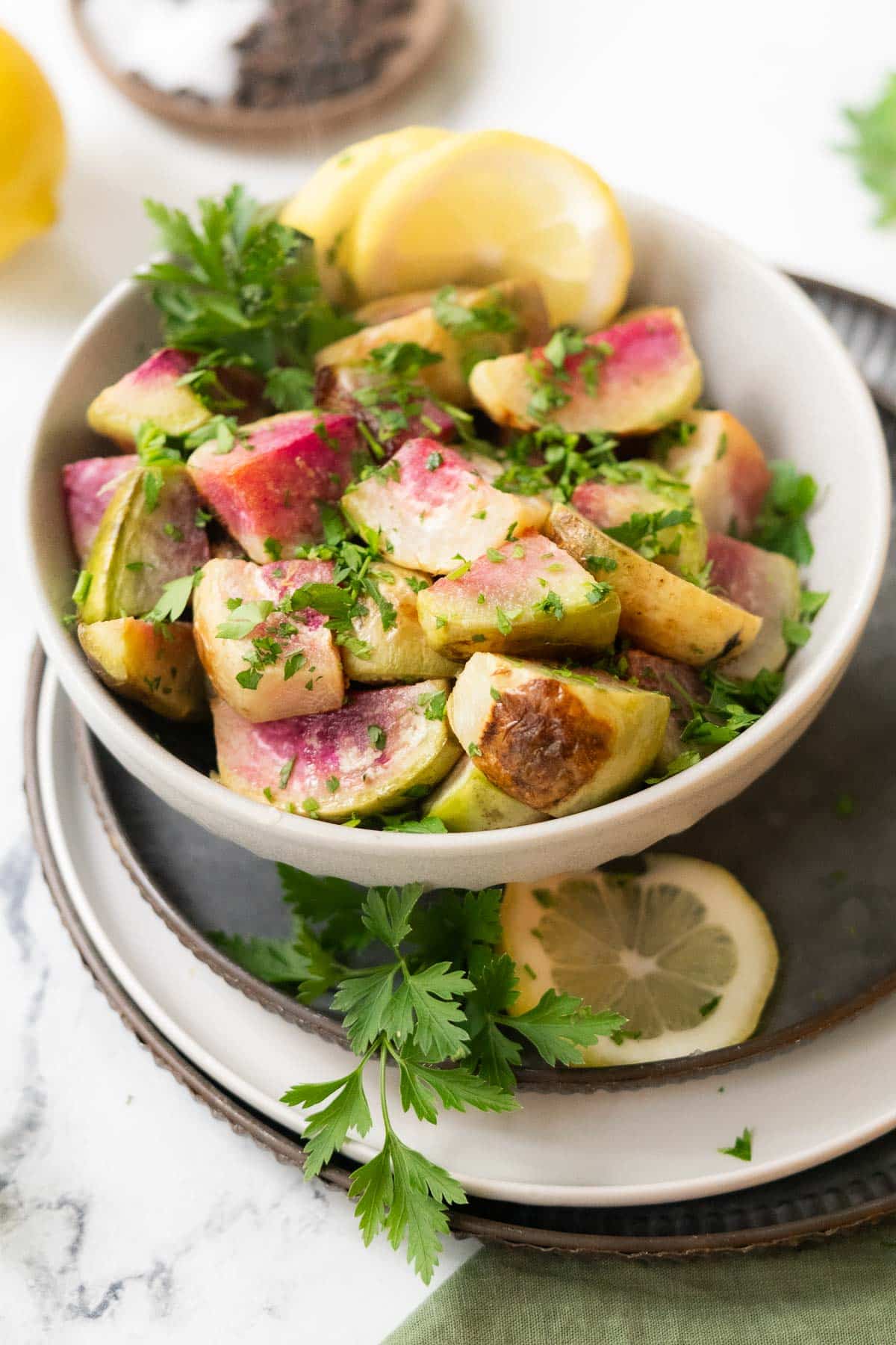 Roasted watermelon radish in a bowl with fresh parsley and slices of lemon.