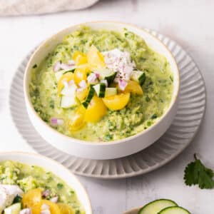 Cucumber Gazpacho topped with slices of tomatoes and cream served in a bowl placed on the table.
