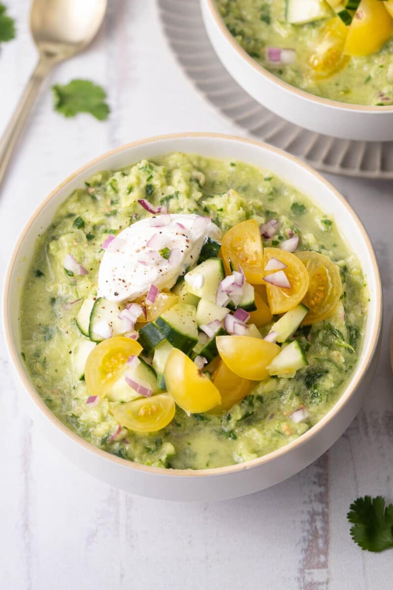 Cucumber Gazpacho topped with tomatoes and cream served in a bowl.