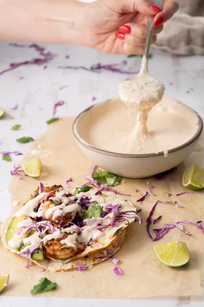 Baja sauce in a soup bowl and a taco with shrimp drizzled with Baja sauce served on the table.