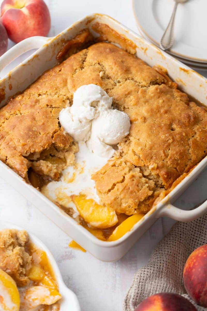 Peach Cobbler in a baking dish topped with vanilla ice cream.