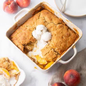 Peach cobbler in a baking dish topped with vanilla ice cream.