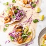 Tacos filled with shrimp and shredded purple cabbage drizzled with Baja sauce.