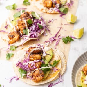 Tacos filled with shrimp and shredded purple cabbage drizzled with Baja sauce.