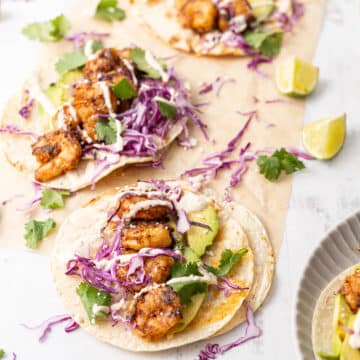 Tacos filled with shrimp and shredded purple cabbage drizzled with Baja sauce.