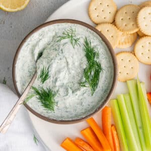 Greek yogurt dill sauce in a small bowl, with crackers, carrot batons, and sprigs.