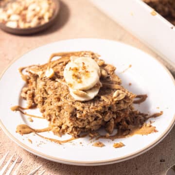 A portion of Baked Oatmeal Peanut Butter topped with slices of banana and nuts drizzled with peanut sauce served on a plate.
